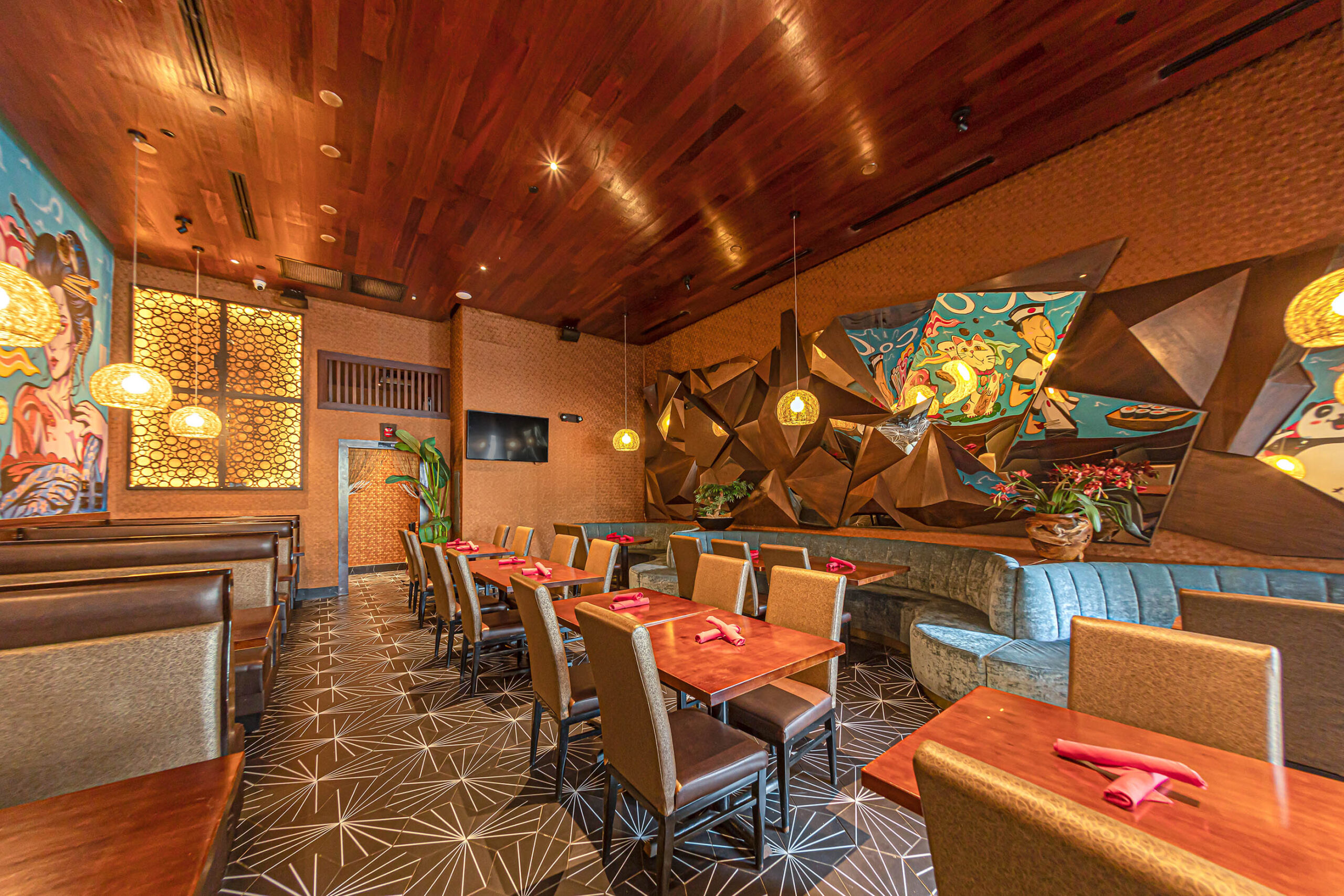 Modern dining room of Coco Restaurant with wooden tables, blue velvet booths, and geometric 3D wall art with murals.