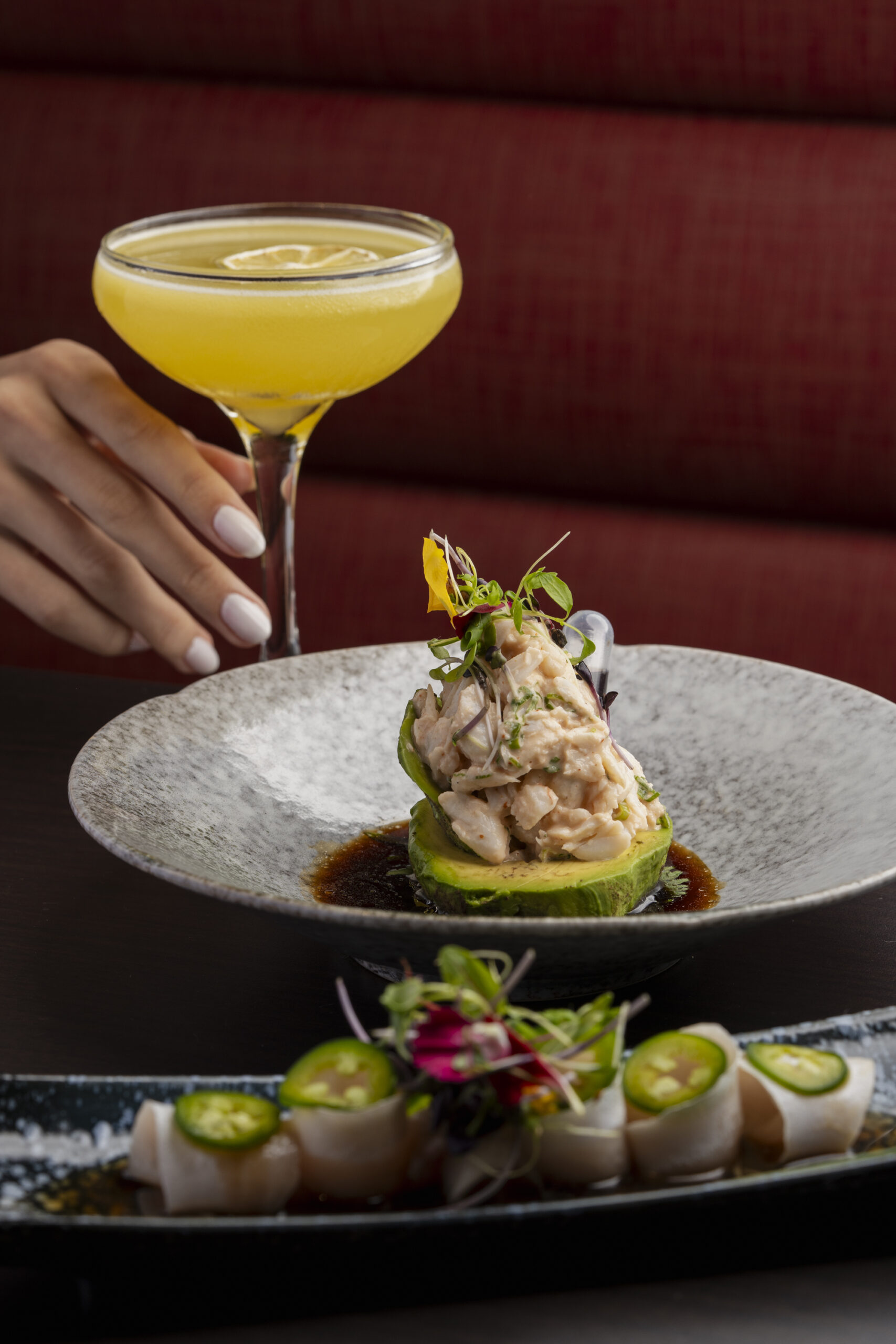 Yellow cocktail in a coupe glass served with crab avocado salad and yellowtail jalapeño crudo.