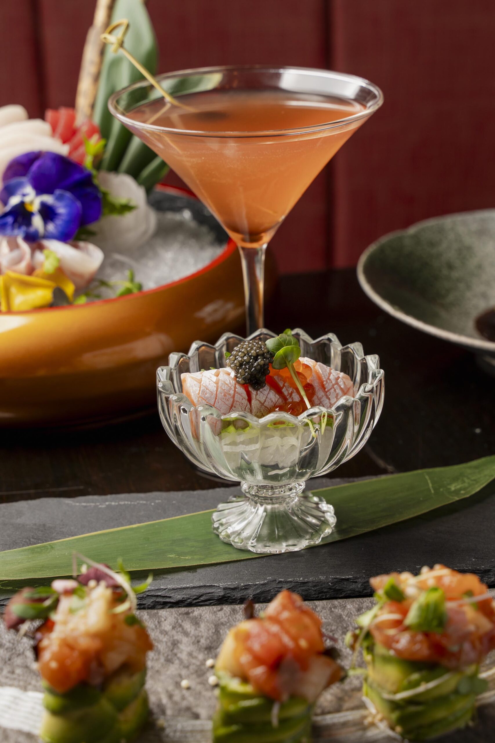 Yellow cocktail in a coupe glass served alongside a crab avocado salad and yellowtail jalapeño crudo.