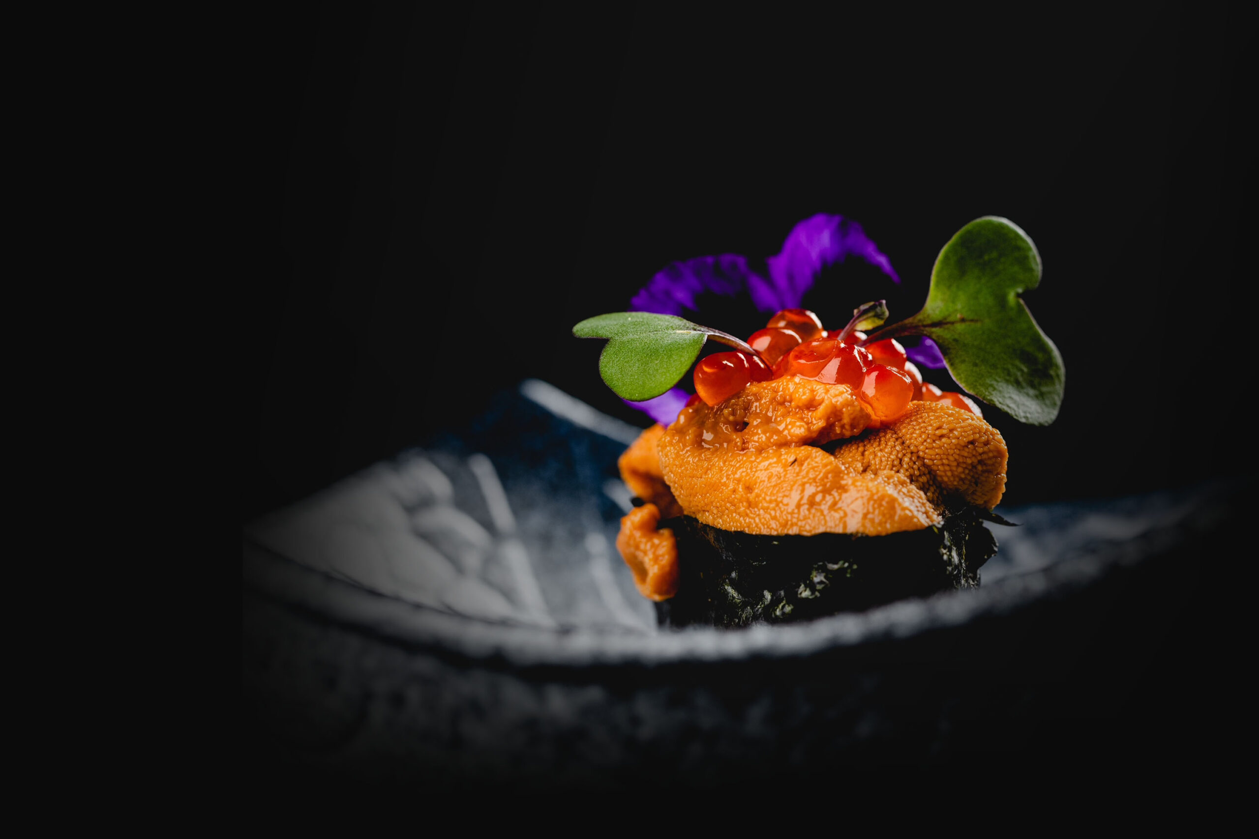Fresh Uni and Ikura gunkan-maki sushi topped with orange sea urchin, glistening red salmon roe, and a purple edible flower garnish