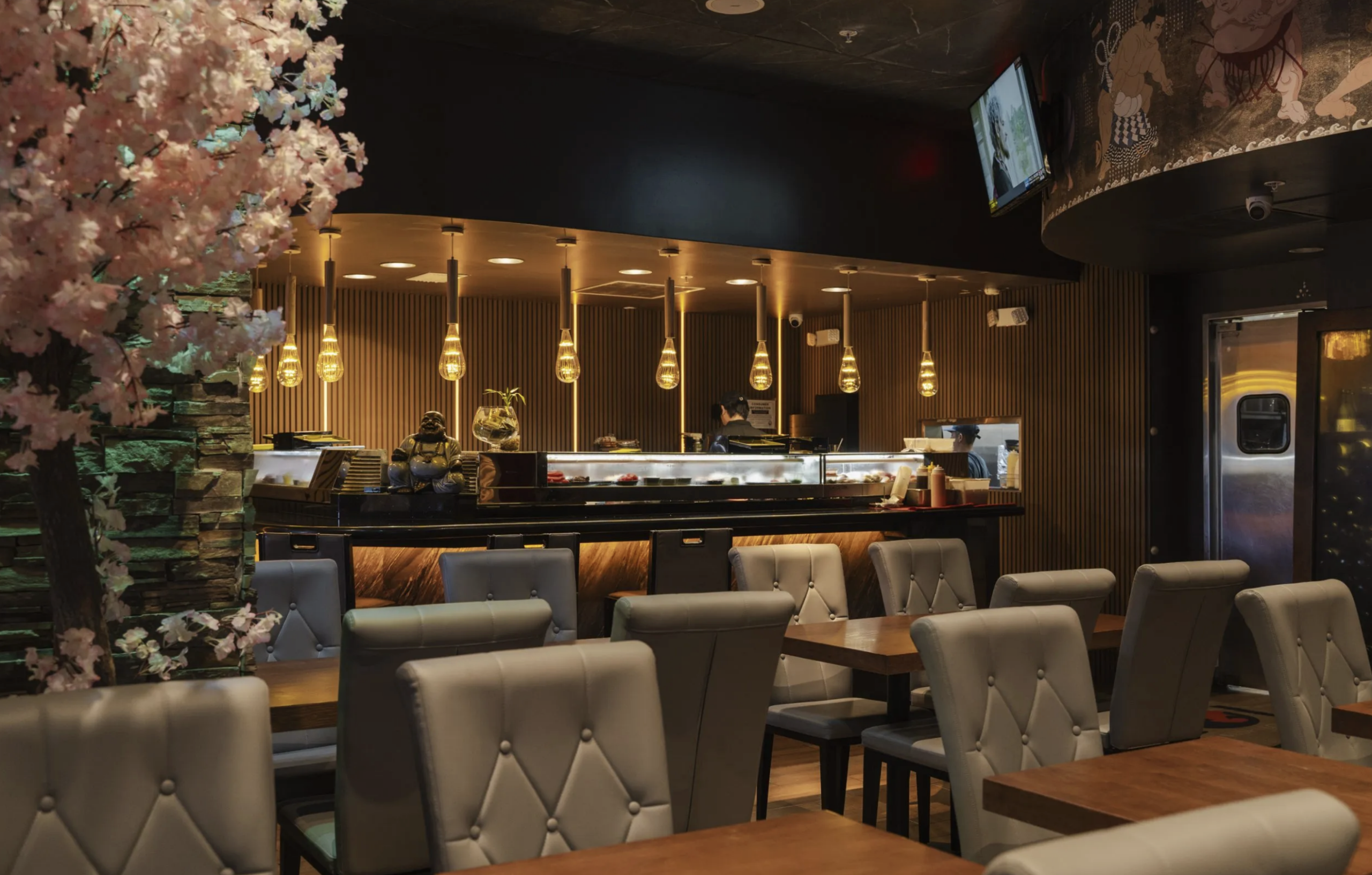 Interior view of Koi Restaurant featuring a dark wood sushi bar, black tufted bar stools, and a warm lit back-bar.