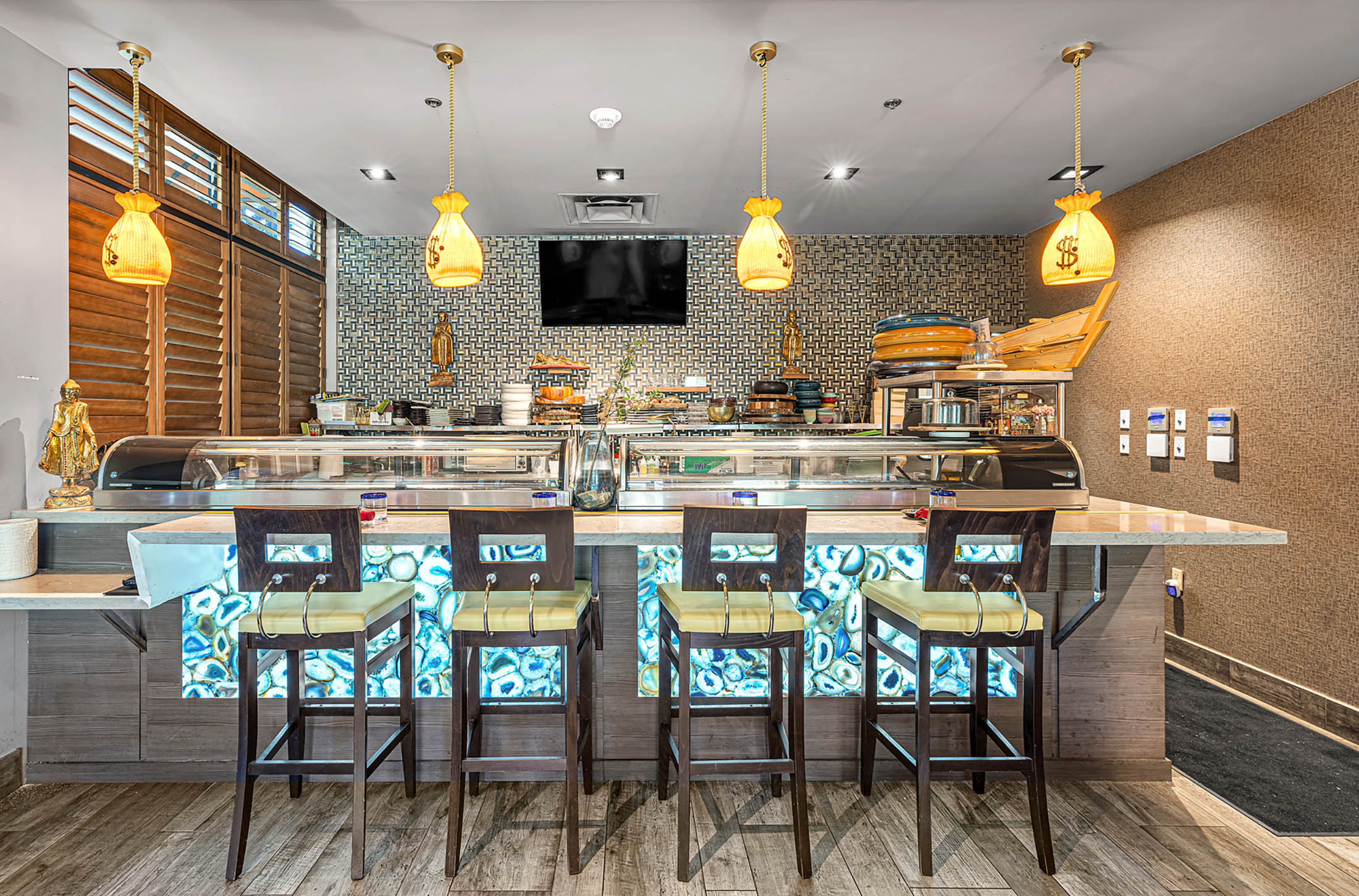 Sushi bar at Yakitori Sake House Delray featuring four wooden bar stools and a counter with glowing blue geode-patterned panels
